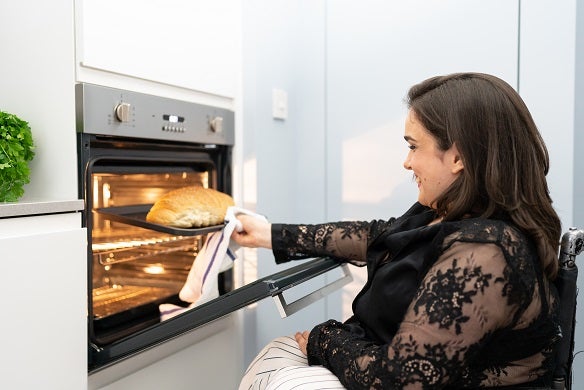 Woman in a wheelchair placing loaf of bread in an oven