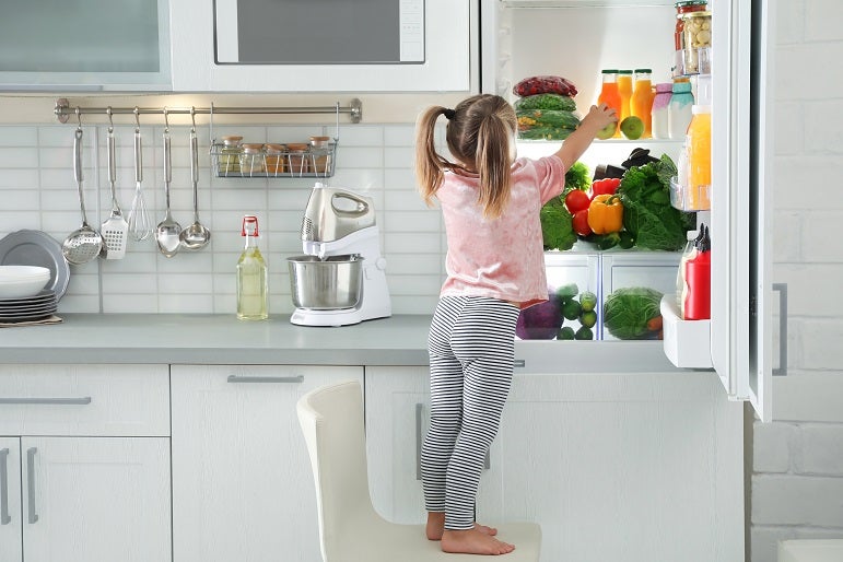 Caucasian blonde little girl taking an apple out of a refrigerator in the kitchen