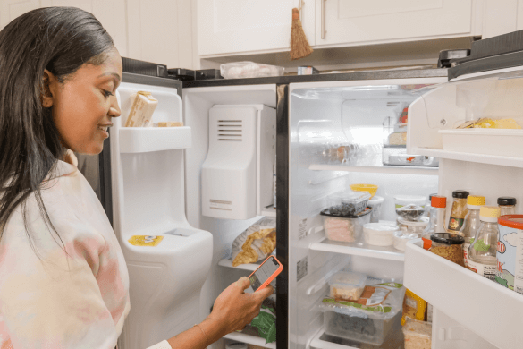 Woman looking at phone whilst holding fridge door open