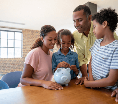 Black family gathered around the kitchen table, putting money into a piggy bank 